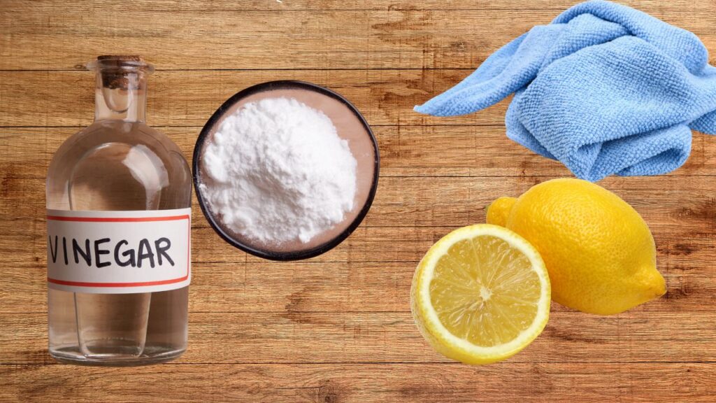 Prirodna sredstva za uklanjanje naslaga kamenca: sirće, soda bikarbona, limun i mikrofiber krpa na drvenoj podlozi.