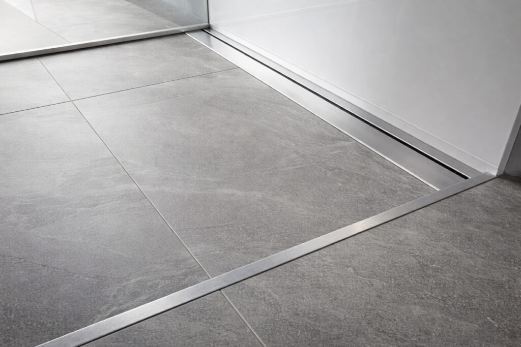 Podna aluminijumska lajsna ugrađena na prelazu keramičkih pločica i tuš kabine u modernom kupatilu